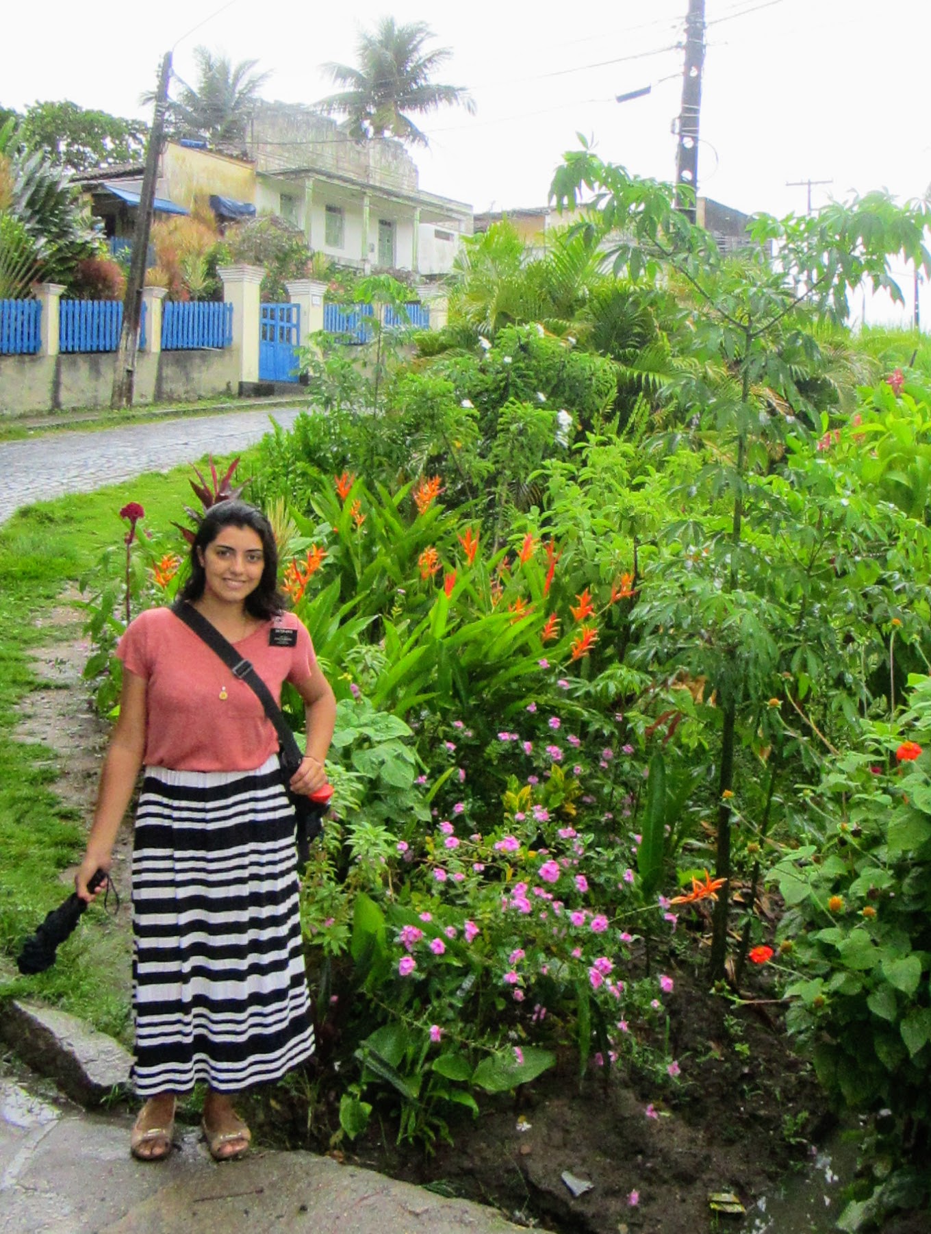 Sister Arece standing outside near the street in front of lush tropical foliage and flowers.